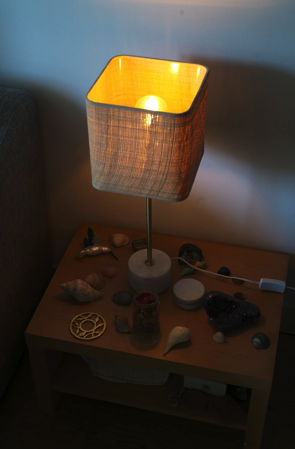 Lampe de chevet allumée au-dessus d'une table couverte de coquillages, de galets et d'une géode violette
